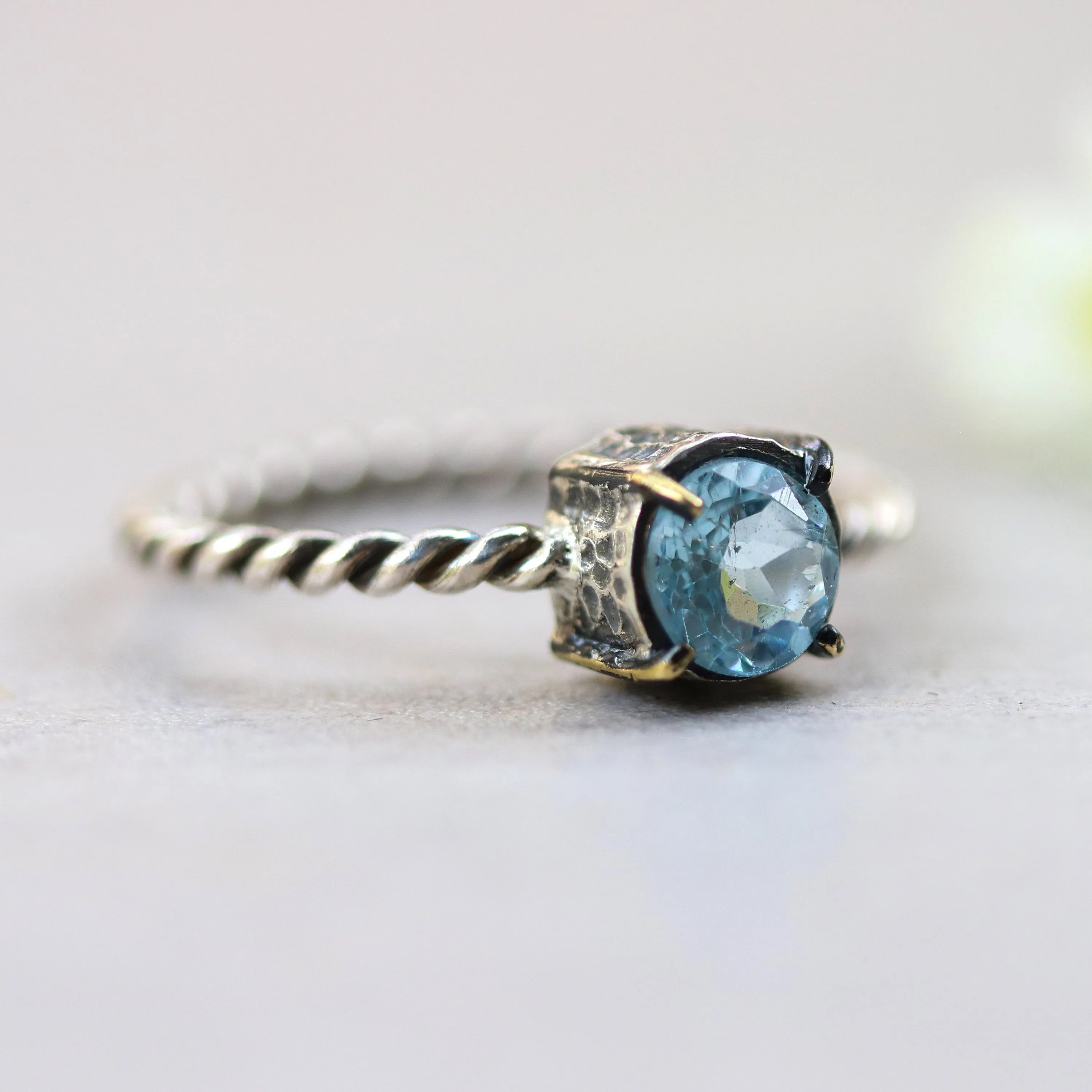 Round faceted blue topaz ring in silver bezel and brass prongs setting with sterling silver twist design band